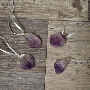 May include: Four amethyst crystal ornaments with silver wire loops and white ribbon hangers. The crystals are various shapes and sizes.