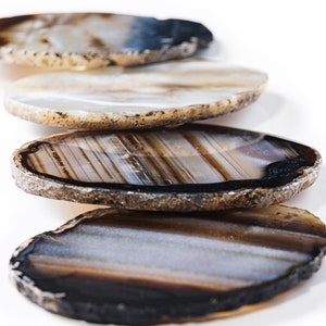May include: Four agate coasters in various shades of brown, white, and black. The coasters are round and have a natural, polished edge.