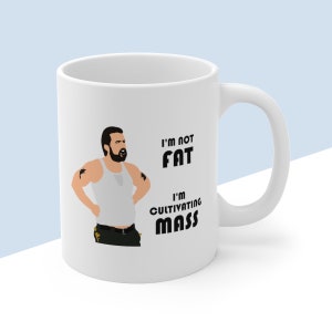 May include: White ceramic mug with a cartoon illustration of a man with a beard and a white tank top. The text on the mug reads "I'm not fat, I'm cultivating mass."
