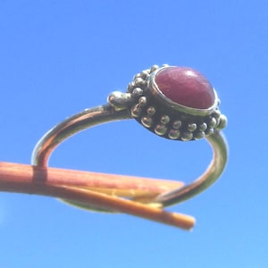 Puede incluir: Un anillo de plata con una piedra preciosa cabujón redonda de color rojo intenso engastada en un bisel. El engaste está decorado con una serie de pequeñas esferas o gránulos de plata en relieve que rodean la base de la piedra, creando una textura.