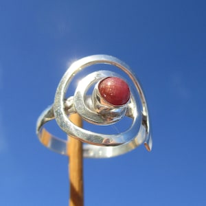 Peut inclure: Une bague en argent avec un motif en spirale et une pierre précieuse rose au centre.