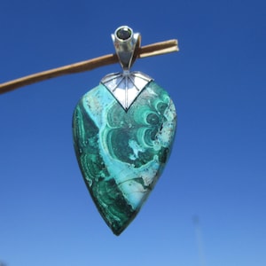 Può includere: Un ciondolo d'argento con una pietra di malachite verde e blu a forma di cuore con una pietra verde più piccola in cima.