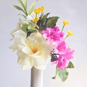 May include: A white vase with a textured surface holds a bouquet of paper flowers. The bouquet includes white, pink, and yellow flowers. The text "Vivid 16" is printed below the vase.
