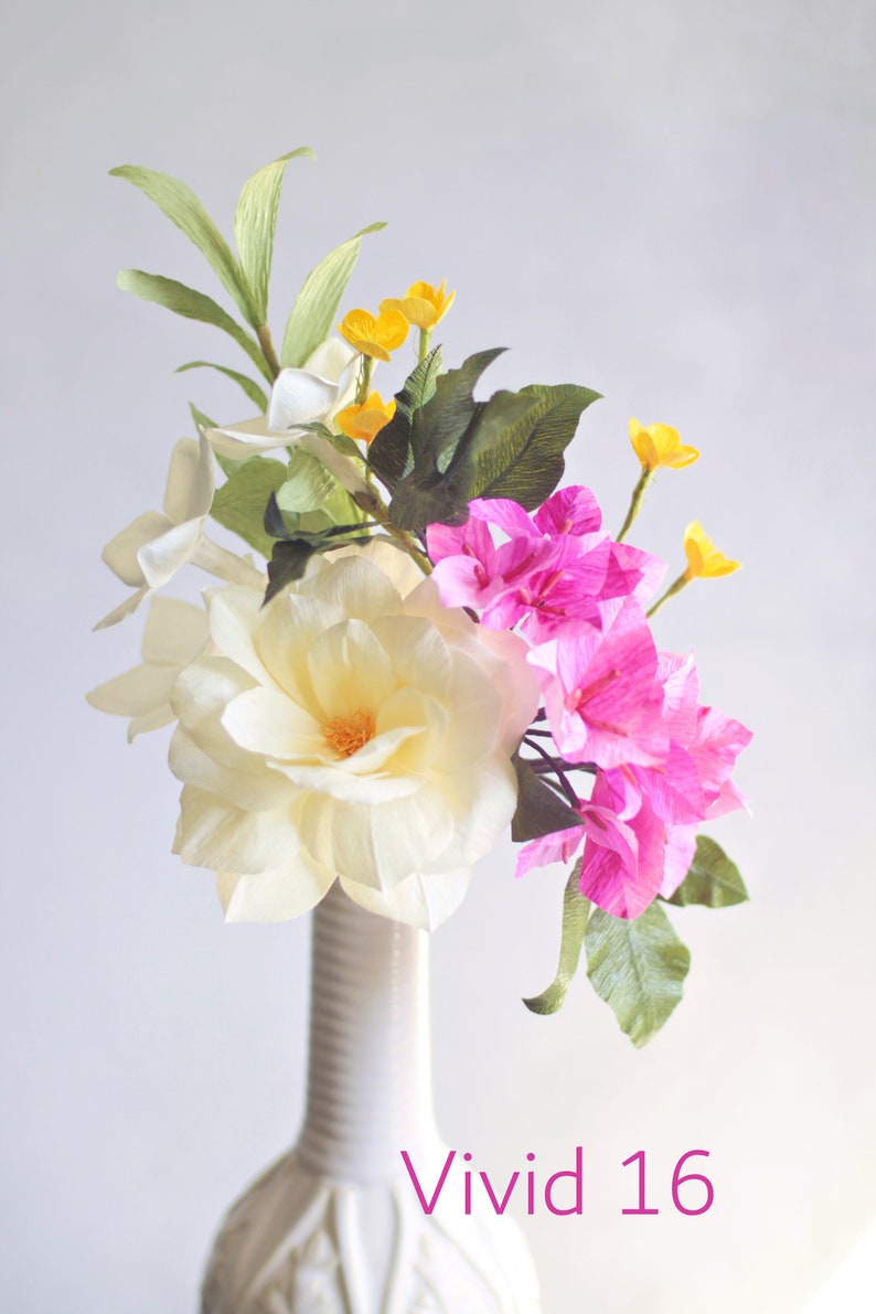 May include: A white vase with a textured surface holds a bouquet of paper flowers. The bouquet includes white, pink, and yellow flowers. The text "Vivid 16" is printed below the vase.