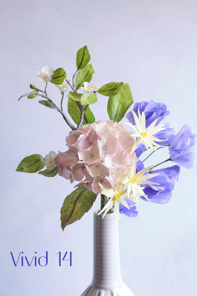 May include: A bouquet of paper flowers in a white vase. The bouquet includes pink hydrangeas, white flowers with yellow centers, and purple flowers. The text "Vivid 14" is visible in the bottom left corner of the image.