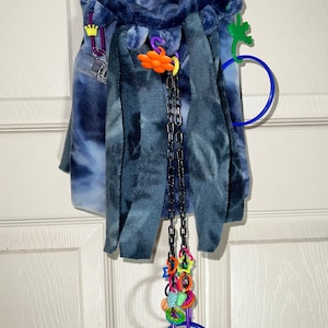 May include: A blue and white tie-dye fabric pouch with a variety of colorful toys hanging from it. The toys include a chain, rings, and a small plastic figure.