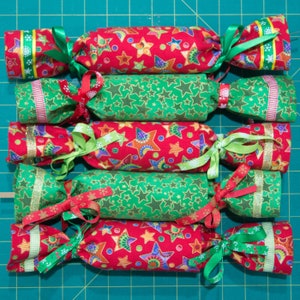 Puede incluir: Seis crackers navideños hechos a mano con tela roja y verde cubierta de estrellas y cinta dorada.