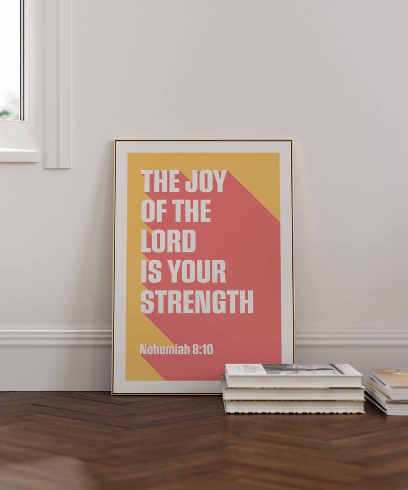 K&ouml;nnte beinhalten: Ein gerahmter Druck mit dem Text "THE JOY OF THE LORD IS YOUR STRENGTH" in Wei&szlig;, vor einem gelben und roten geometrischen Hintergrund. Der Druck wird auf einem Holzboden mit einem Stapel B&uuml;cher in der N&auml;he angezeigt.
