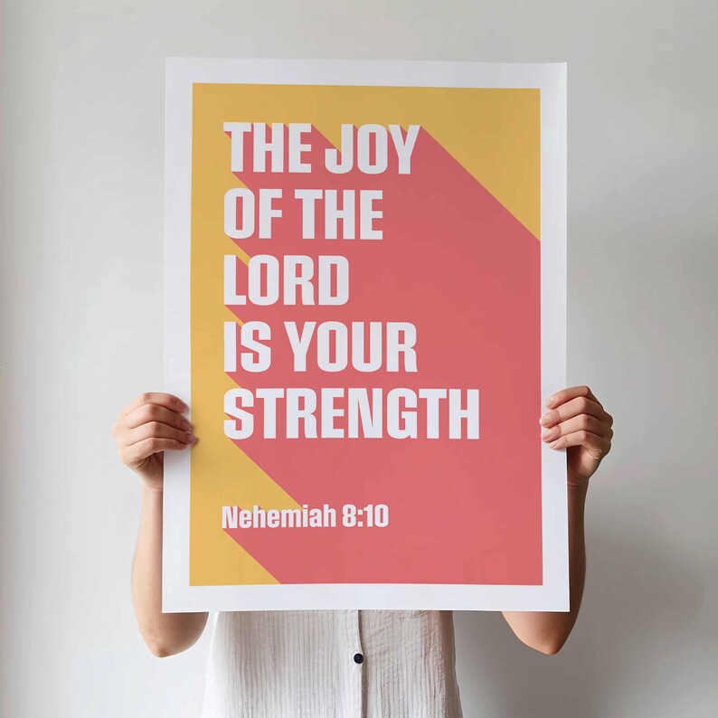 K&ouml;nnte beinhalten: Ein Poster mit dem Text "THE JOY OF THE LORD IS YOUR STRENGTH" in Wei&szlig;, vor einem roten und gelben Hintergrund. Der Text "Nehemiah 8:10" befindet sich unten. Das Poster wird von einer Person gehalten.