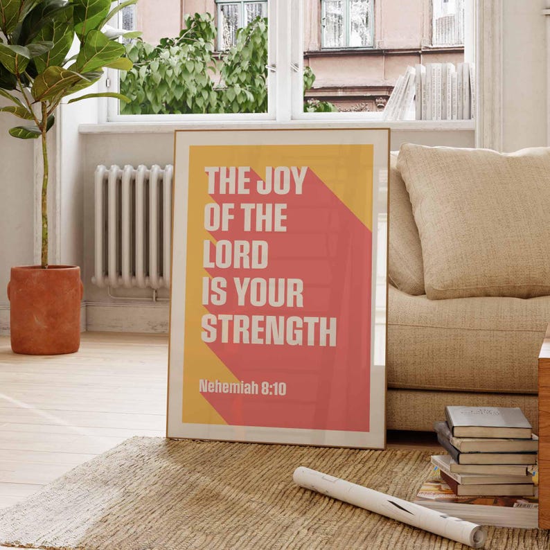 K&ouml;nnte beinhalten: Ein gerahmter Kunstdruck mit dem Text "THE JOY OF THE LORD IS YOUR STRENGTH" in Wei&szlig;, vor einem gelben und roten Hintergrund. Der Druck enth&auml;lt auch den Bibelvers Nehemia 8:10. Das Kunstwerk wird auf einem Teppich pr&auml;sentiert.