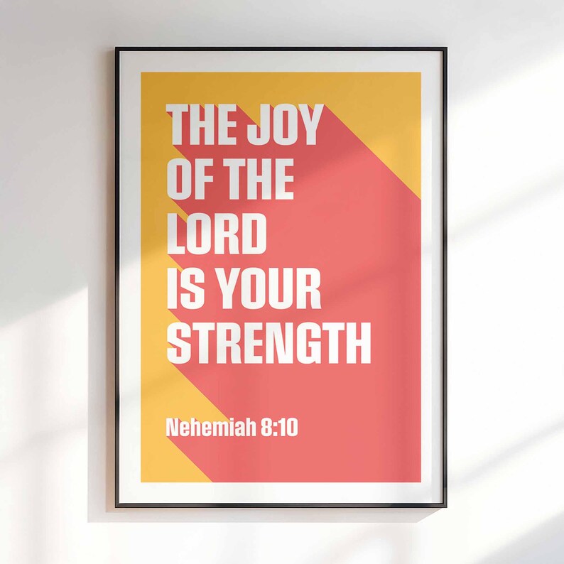 K&ouml;nnte beinhalten: Gerahmtes Poster mit dem wei&szlig;en Text "THE JOY OF THE LORD IS YOUR STRENGTH" auf einem roten und gelben Hintergrund. Das Zitat stammt aus Nehemia 8:10. Das Poster befindet sich in einem schwarzen Rahmen und h&auml;ngt an einer wei&szlig;en Wand.