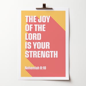 K&ouml;nnte beinhalten: Ein rechteckiger Druck mit dem Text "THE JOY OF THE LORD IS YOUR STRENGTH" in Wei&szlig;, vor einem korallenfarbenen und gelben Hintergrund. Der Text hat einen langen Schatteneffekt. Der Bibelvers "Nehemia 8:10" steht unten.