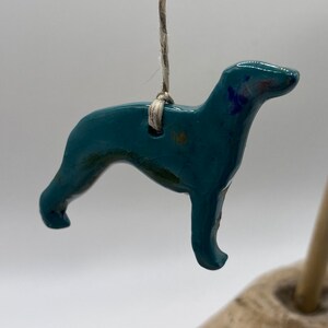 May include: A teal blue ceramic dog figurine hanging from a string. The dog is in a running pose with its head turned to the side.