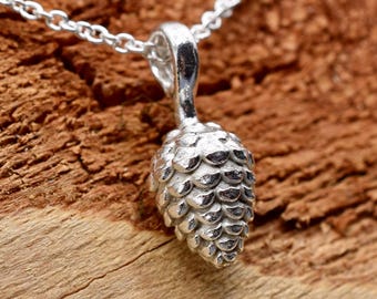 May include: A silver-toned pendant shaped like a small pinecone, suspended from a delicate matching silver-toned chain. The pendant features a detailed, textured surface mimicking the scales of a pinecone, with a polished metallic finish.
