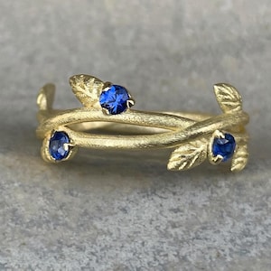 May include: A gold ring with three blue sapphires set in a delicate leaf design.