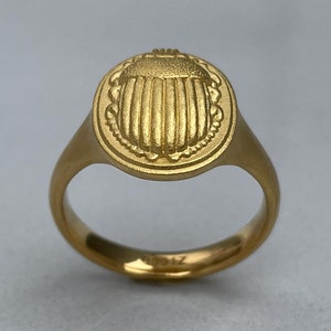 May include: A gold ring featuring a raised scarab beetle design. The ring is oval shaped and has a smooth band.