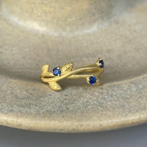 May include: A gold ring with a delicate design of intertwined branches and four blue sapphires.