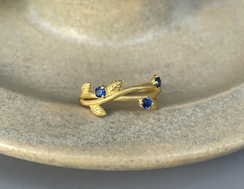 May include: A gold ring with a delicate design of intertwined branches and four blue sapphires.