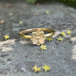 May include: A gold ring with a delicate flower design. The flower is made of metal and has a textured surface.