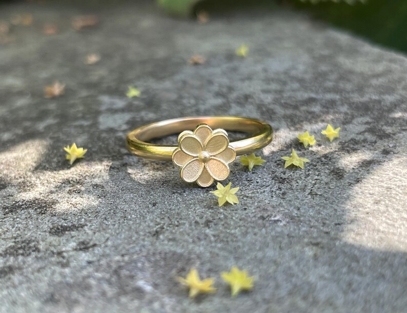 May include: A gold ring with a delicate flower design. The flower is made of metal and has a textured surface.