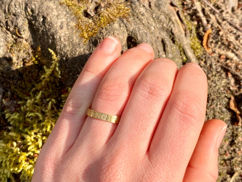 K&ouml;nnte beinhalten: Ein goldener Ring mit der Gravur "VINCIT" auf der Band.
