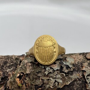 May include: A gold ring with an oval-shaped design featuring a raised, detailed image of a scarab beetle.