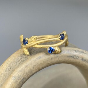 May include: A gold ring with three blue sapphires set in a delicate branch design.