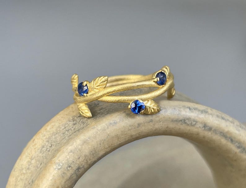 May include: A gold ring with three blue sapphires set in a delicate branch design.