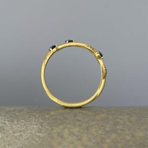 May include: A gold ring with three small blue gemstones set into the band.