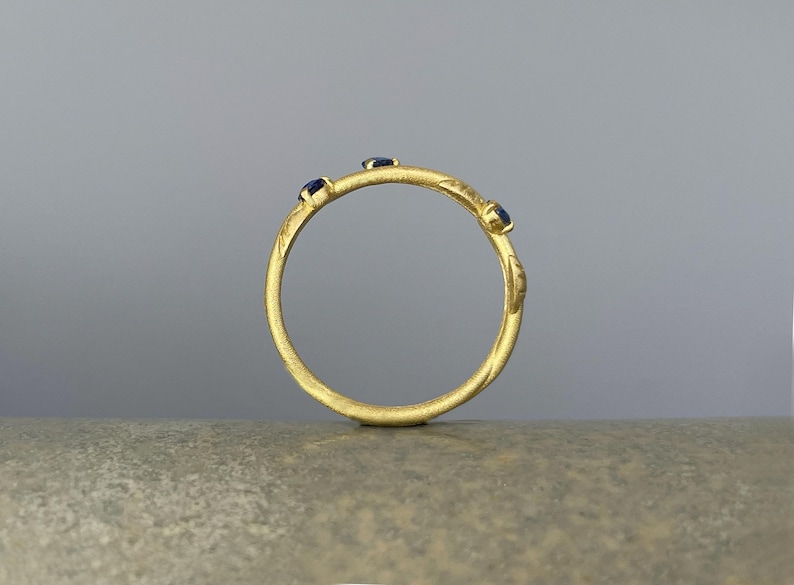 May include: A gold ring with three small blue gemstones set into the band.