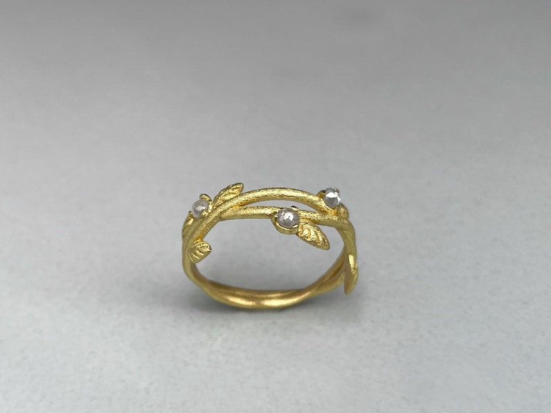 May include: A gold ring with a vine-like design. The ring has small, clear gemstones and leaf details. The band is smooth and the design is inspired by nature. The ring is a piece of jewellery.