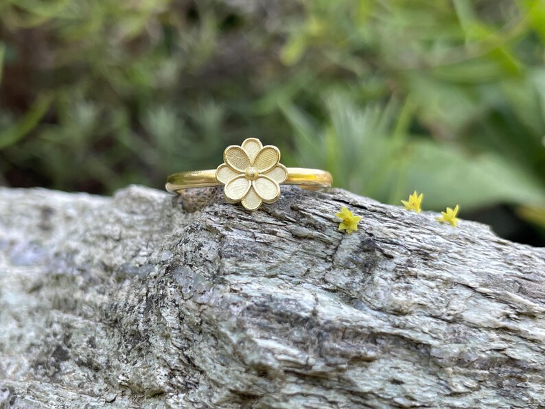 May include: A gold ring with a white flower design. The ring is sitting on a piece of wood.