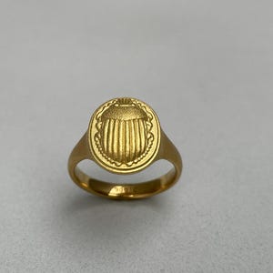May include: A gold ring featuring a round, raised design of a scarab beetle.