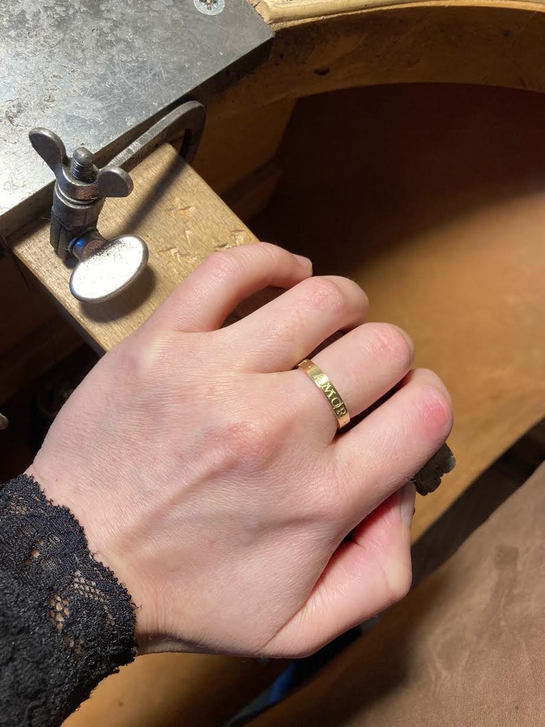 K&ouml;nnte beinhalten: Ein goldener Bandring mit der Gravur "AMOR".