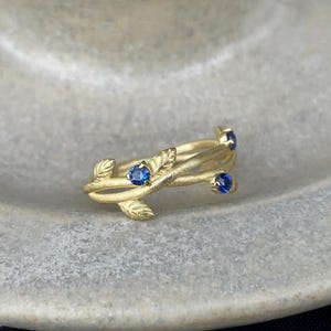 May include: A gold ring with a delicate vine design and four blue sapphires.