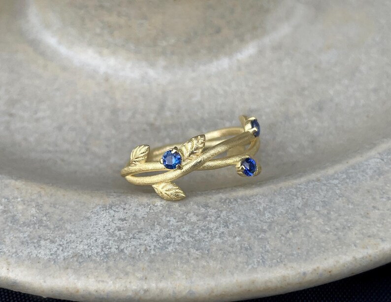 May include: A gold ring with a delicate vine design and four blue sapphires.