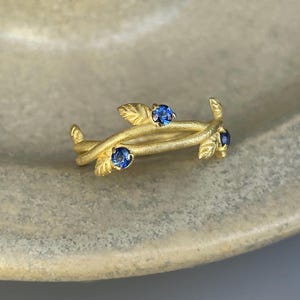 May include: A gold ring with a delicate design of intertwined branches and three blue gemstones.