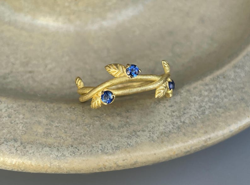 May include: A gold ring with a delicate design of intertwined branches and three blue gemstones.