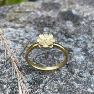 May include: A gold ring with a delicate flower design. The flower is raised and has a slightly textured surface.