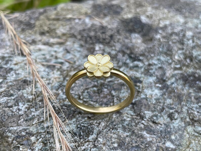 May include: A gold ring with a delicate flower design. The flower is raised and has a slightly textured surface.