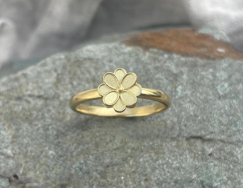 May include: A gold ring with a white flower design. The flower has five petals and a small center.