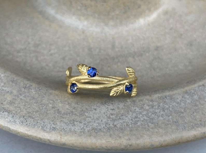May include: A gold ring with three blue sapphires set in a delicate leaf design.