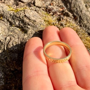 K&ouml;nnte beinhalten: Ein goldener Bandring mit der Gravur "OMNIA" auf der Au&szlig;enseite.