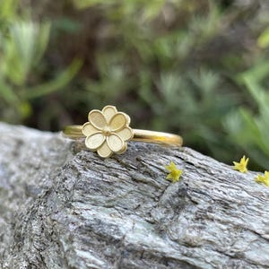 May include: A gold ring with a delicate flower design. The ring is sitting on a piece of weathered wood.