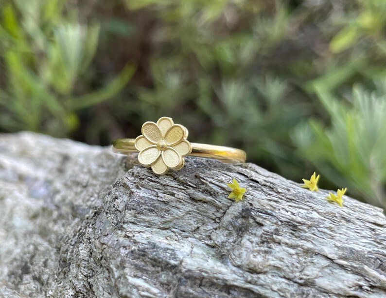 May include: A gold ring with a delicate flower design. The ring is sitting on a piece of weathered wood.