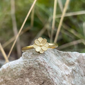 May include: A gold ring with a delicate flower design. The flower is made of multiple petals and has a textured surface.