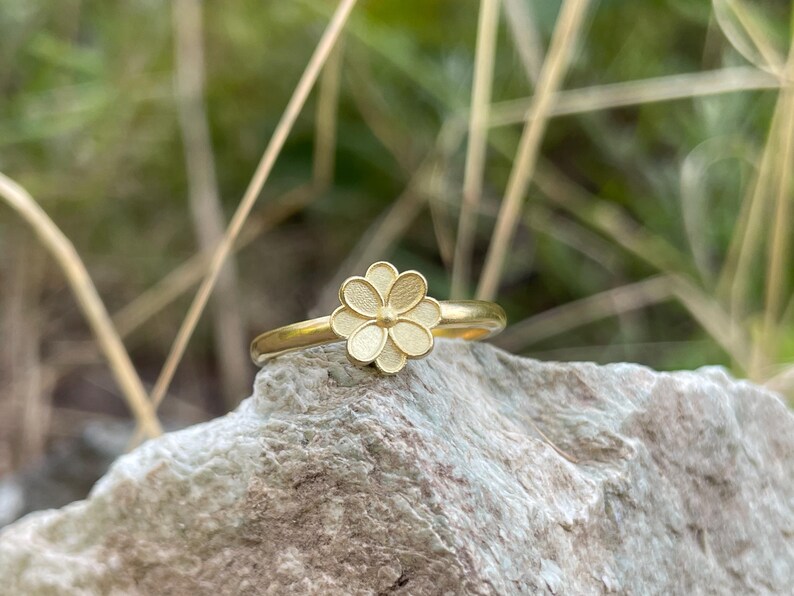 May include: A gold ring with a delicate flower design. The flower is made of multiple petals and has a textured surface.