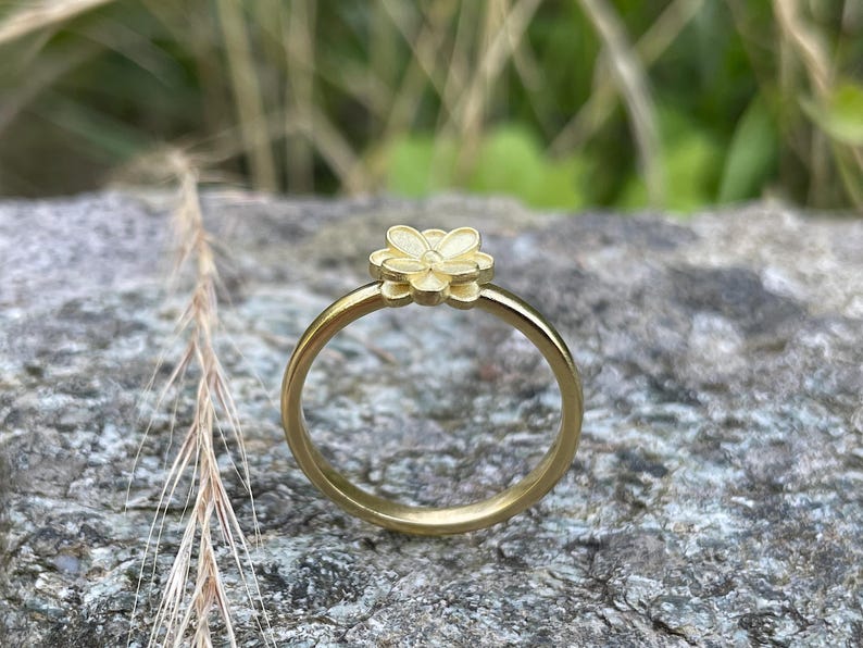 May include: A gold ring with a delicate flower design. The ring is simple and elegant, perfect for everyday wear.