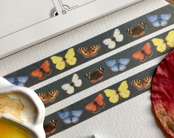 May include: A roll of washi tape with a repeating pattern of colorful butterflies on a dark gray background.