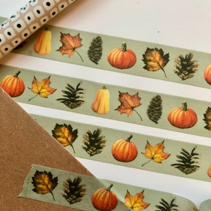 May include: A roll of washi tape with a green background and a repeating pattern of pumpkins, pinecones, and fall leaves.